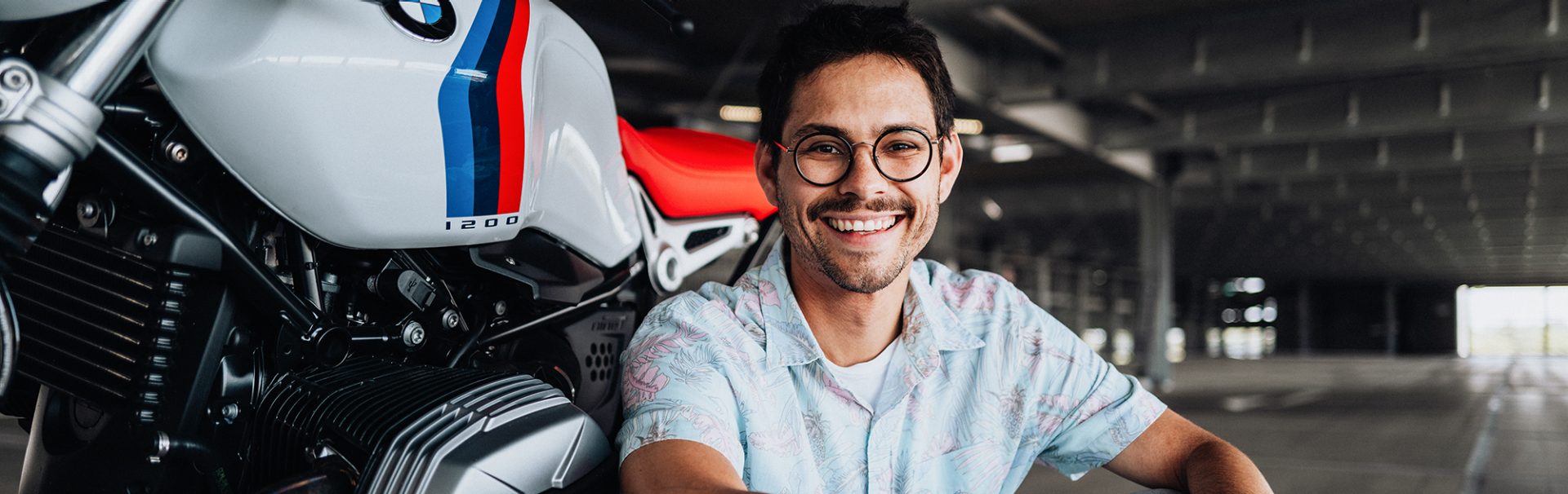 BMW Mitarbeiter sitzt vor einem BMW Motorrad auf dem Boden eines Parkhauses.
