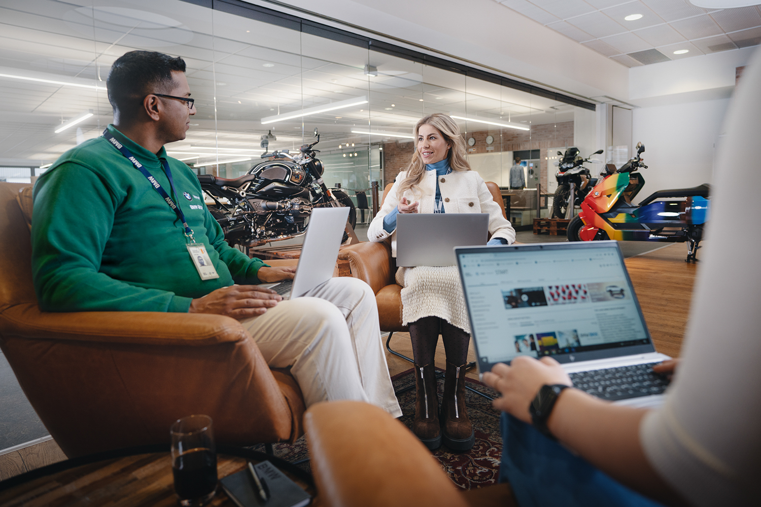 Three colleagues at the BMW Group collaborating in a modern work environment with various BMW Motorcycles in the background.