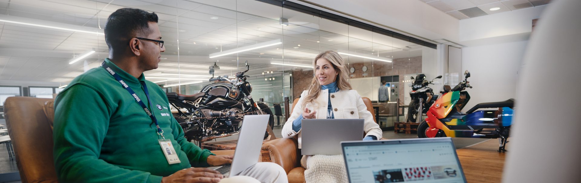 Three colleagues at the BMW Group collaborating in a modern work environment with various BMW Motorcycles in the background.