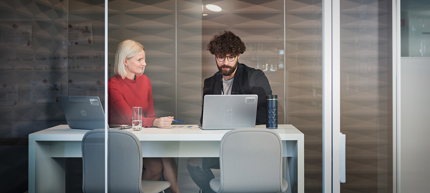 Two colleagues having a development conversation in a modern meeting room with glass walls.