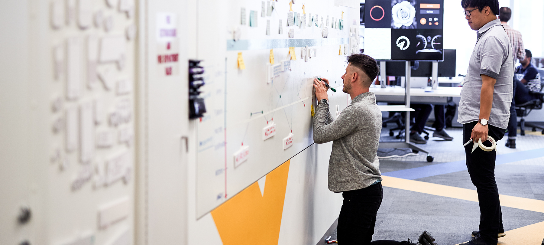 Two colleagues working together on their plans on a whiteboard.