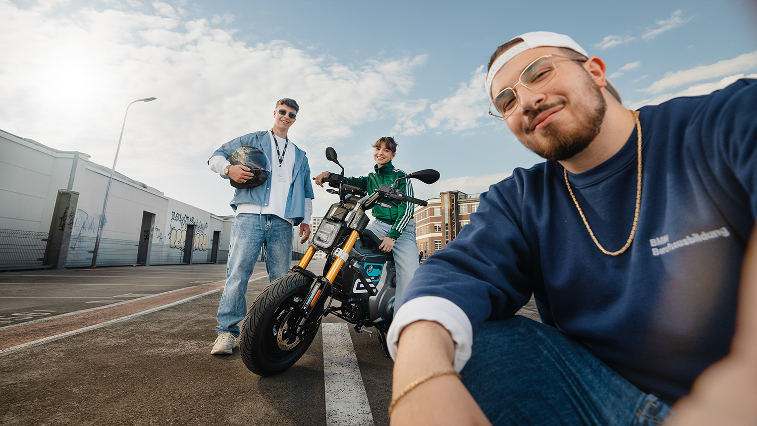 Three apprentices posing with a electric BMW Motorcycle on a parking lot.