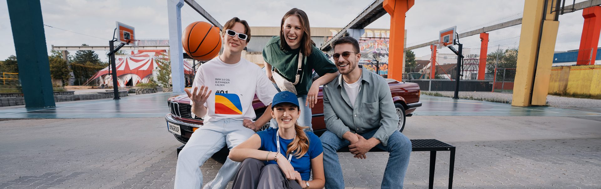 A group of four apprentices enjoying basketball outdoors with a vintage BMW in the background.