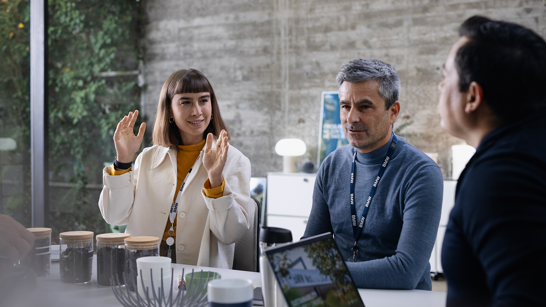 Three colleagues at the BMW Group are having a collaborative conversation in a modern office setting.
