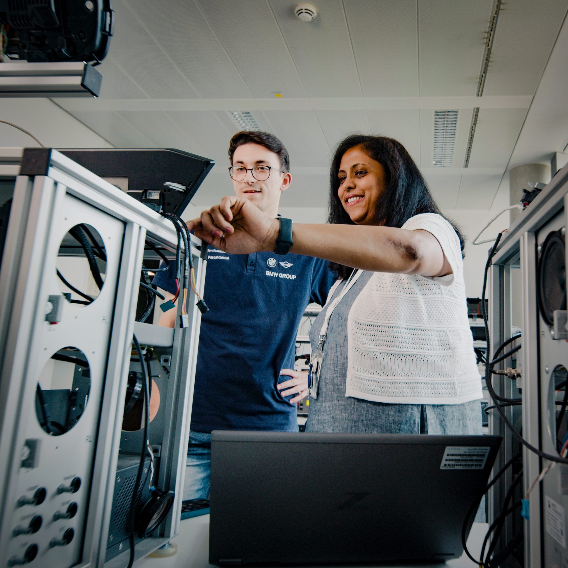The image shows Nisha in exchange with a colleague at a test rack.