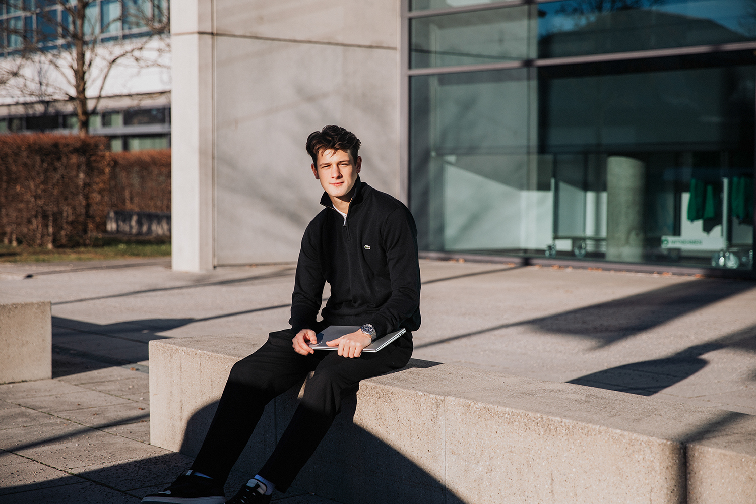 The Dual Student sitting on a beton bench infront of the Campus in Munich