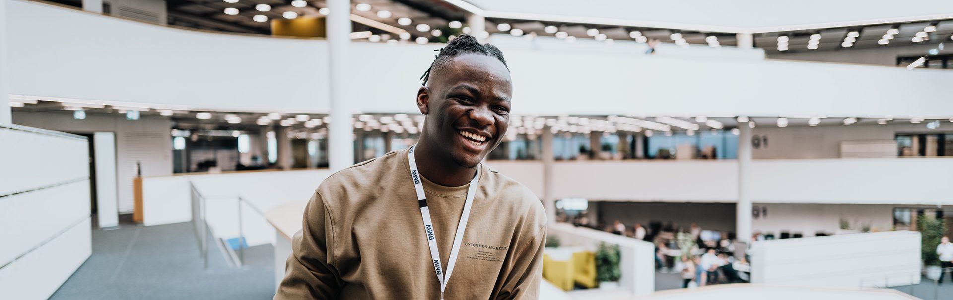 The working student stand in the BMW Research and Innovation centre, smiling at the camera.