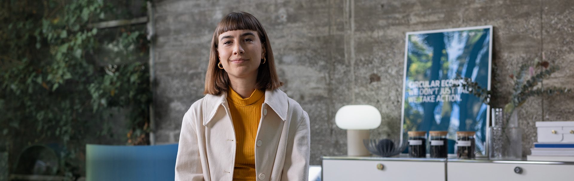 Female employee in sustainability sitting in a modern office environment, smiling at the camera.