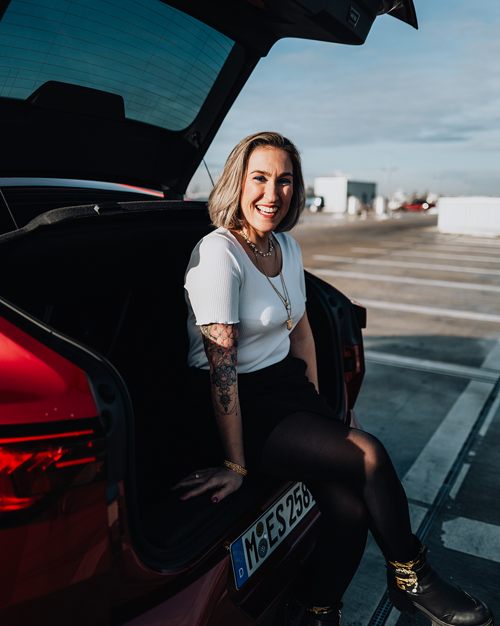 BMW Mitarbeiterin Julia sitzt auf der Ladekante des Kofferraums eines roten BMW X2