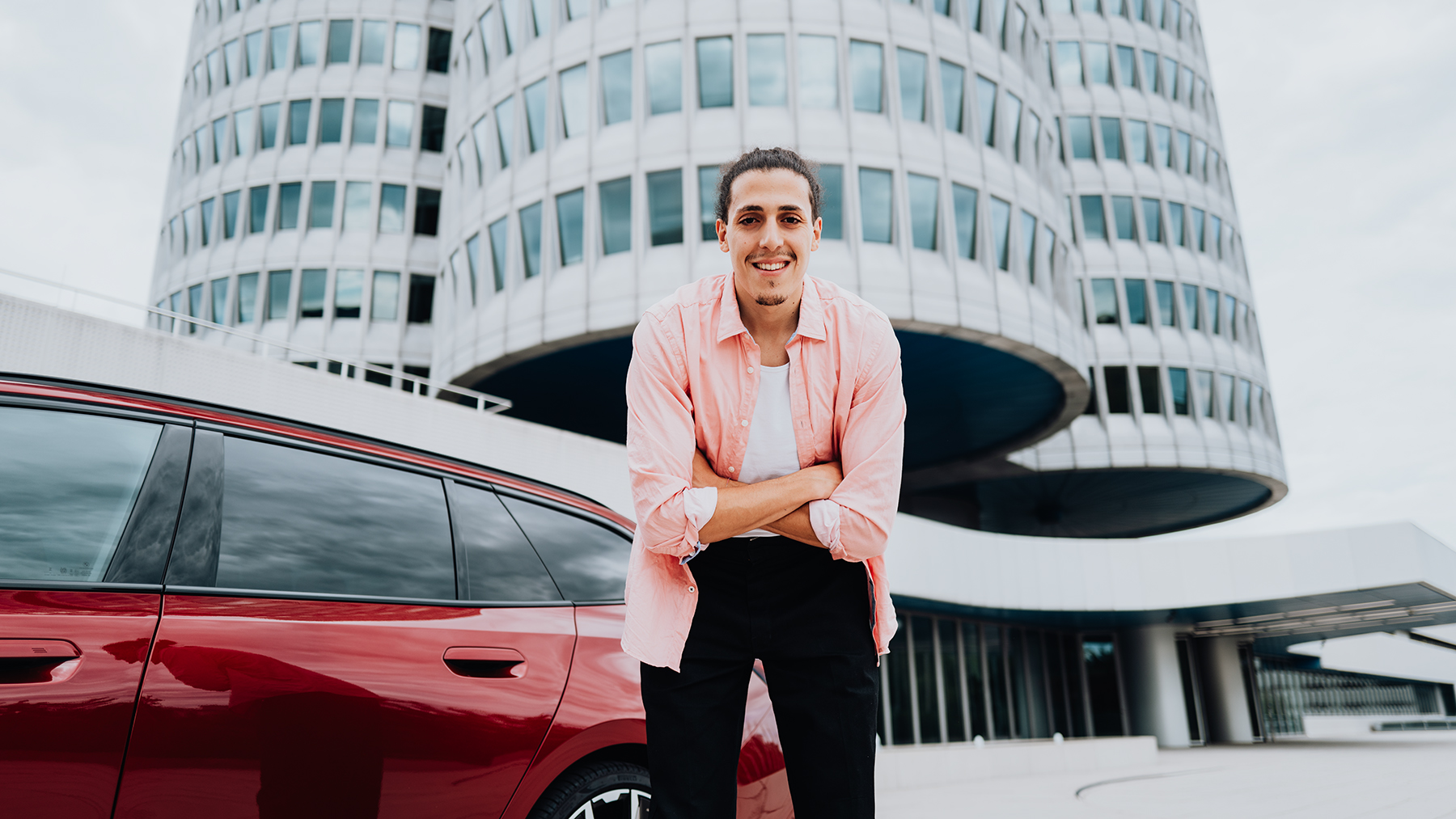 BMW Group employee with the BMW i5 in front of the headquarters building in Munich