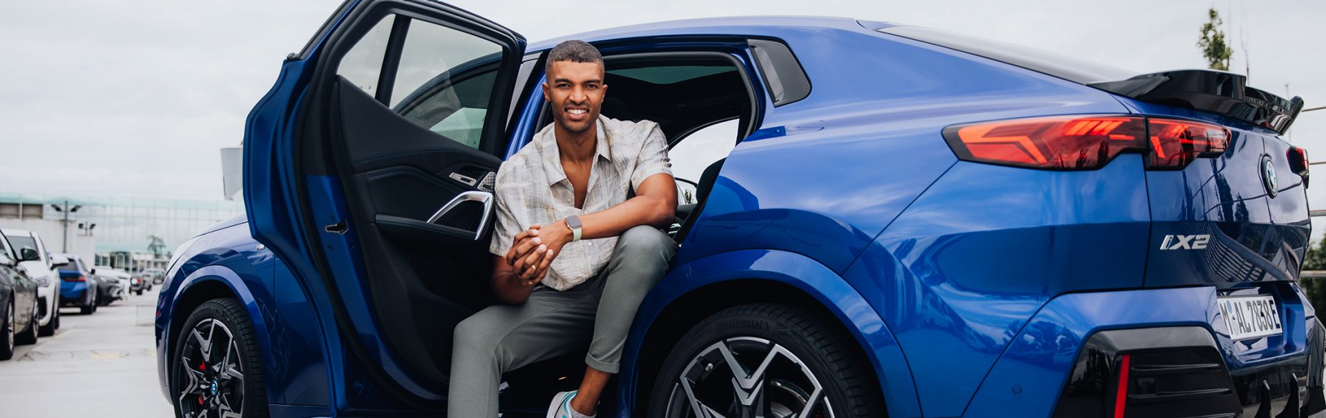 Engineer at the BMW Group sitting on the backseats of a BMW iX2 smiling at the camera.