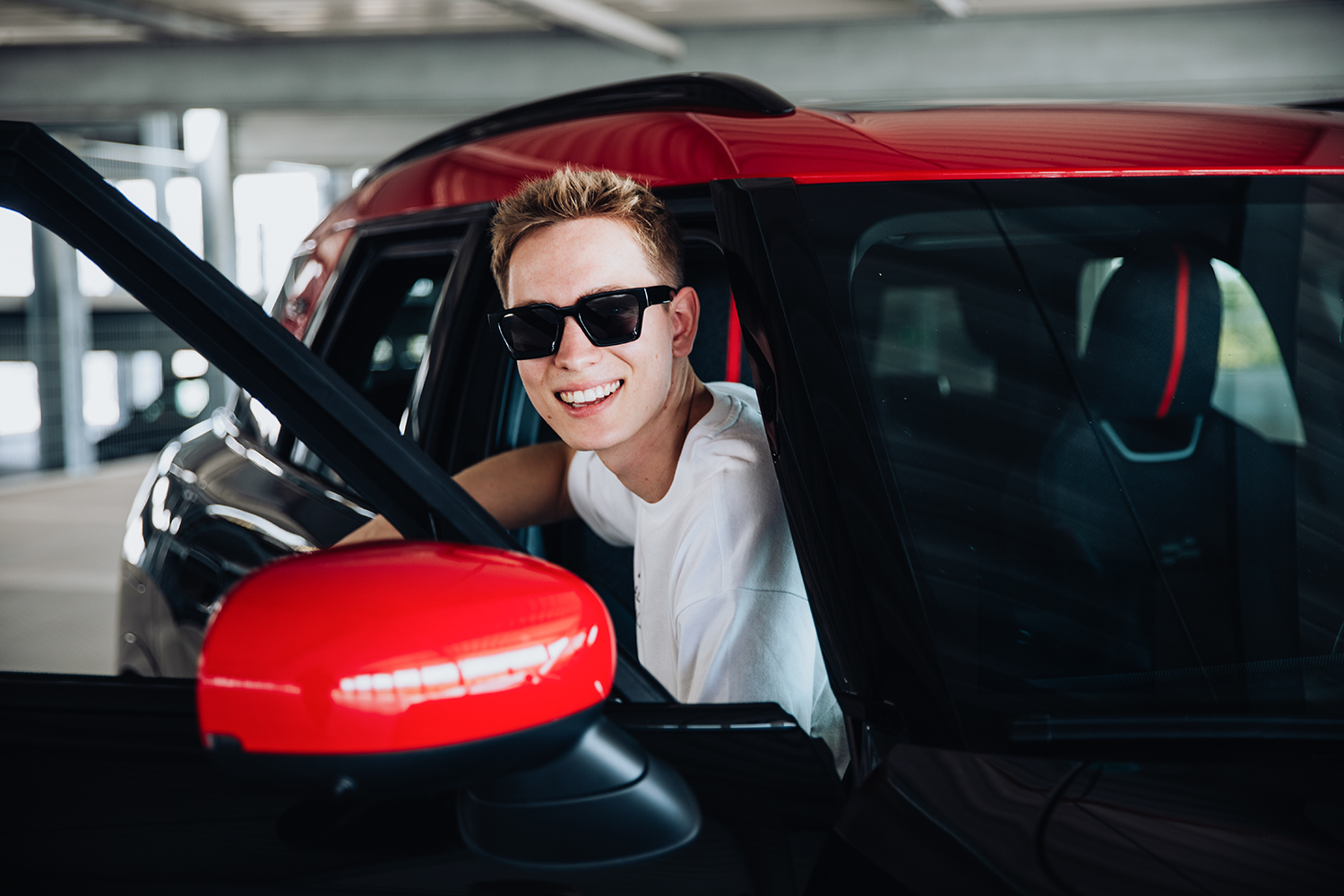 Student sitting in the car with the door open, smiling at the camera.
