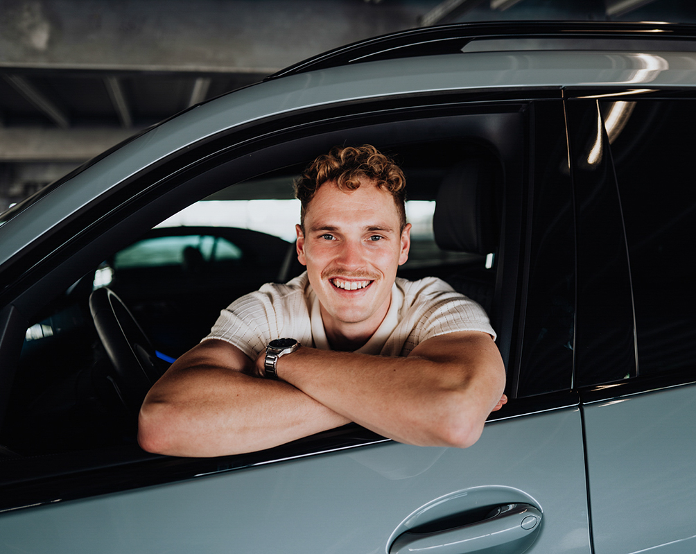 Engineer leaning out of a window of a BMW X7 smiling at the camera.