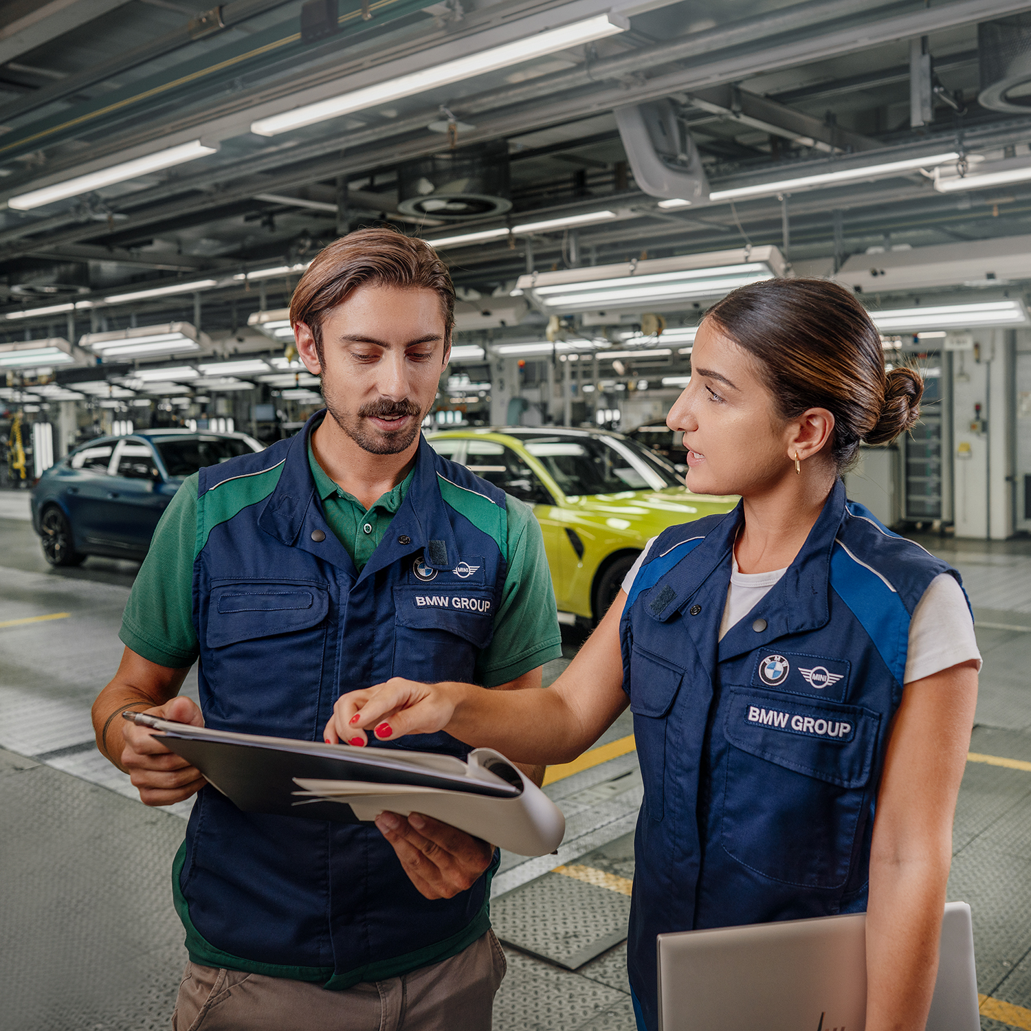 Two colleagues at the BMW Group are talking about documents in a workshop.