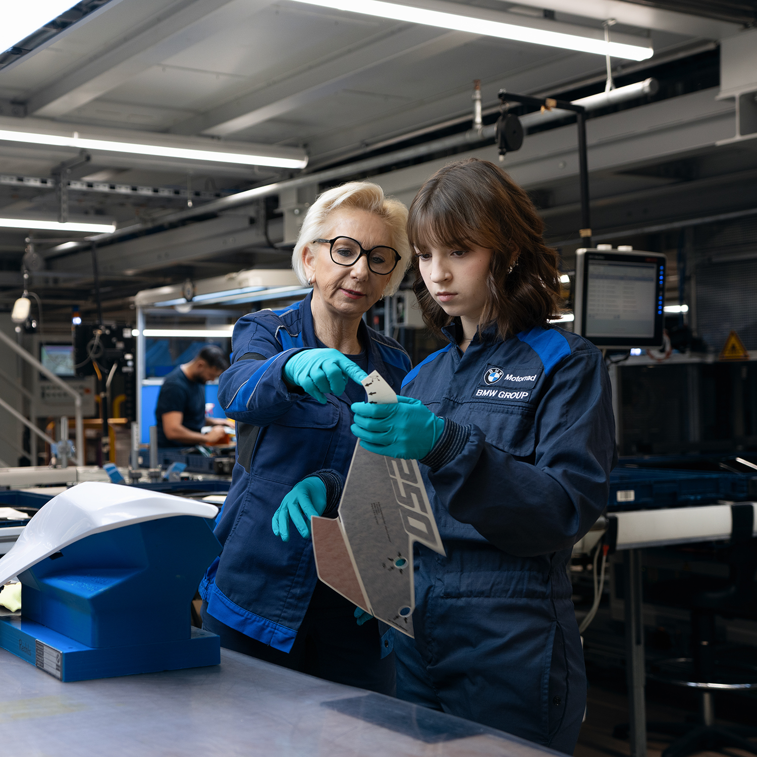 An older colleague explains a process step in the paint shop to a younger colleague
