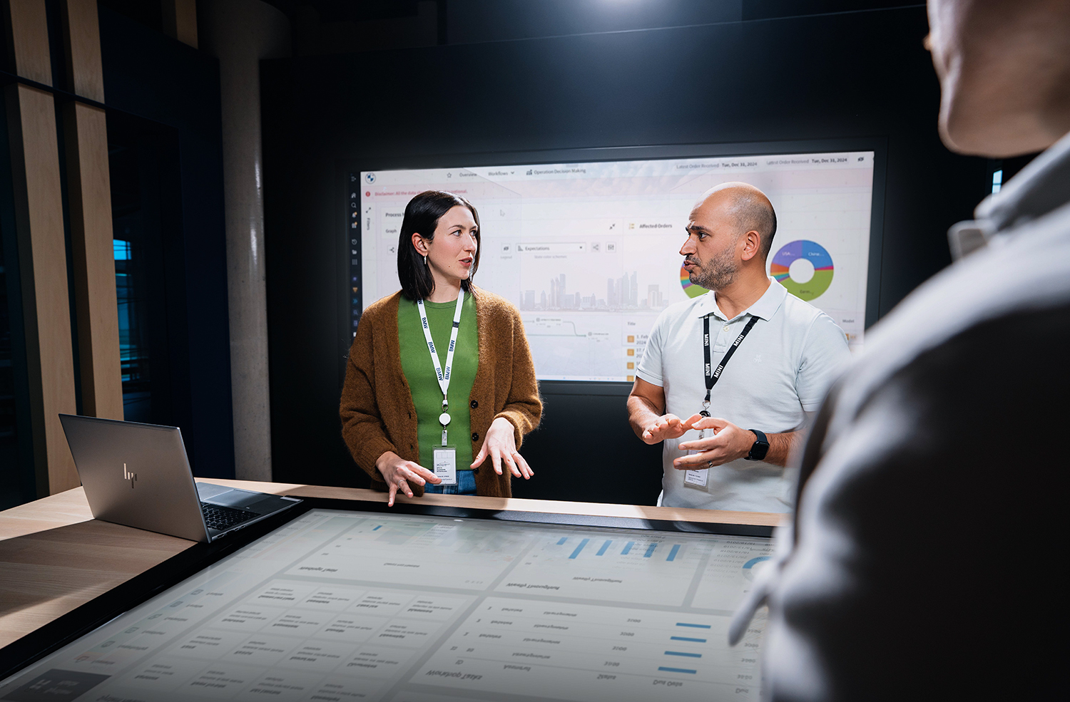Three IT colleagues converse at an interactive table with a large screen as a worktop.