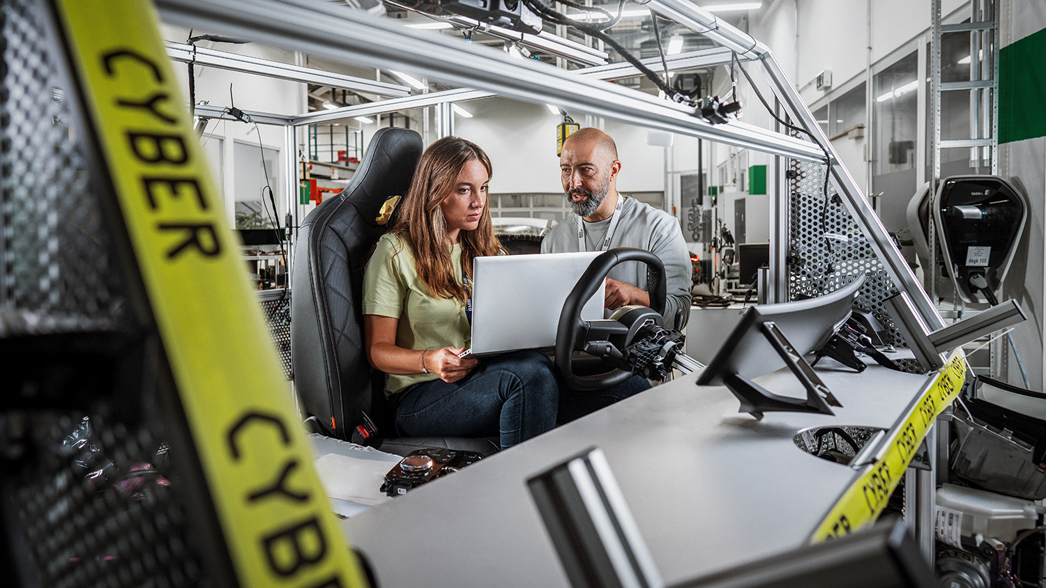 Two BMW Group employees working together on a computer  in a car simulator.