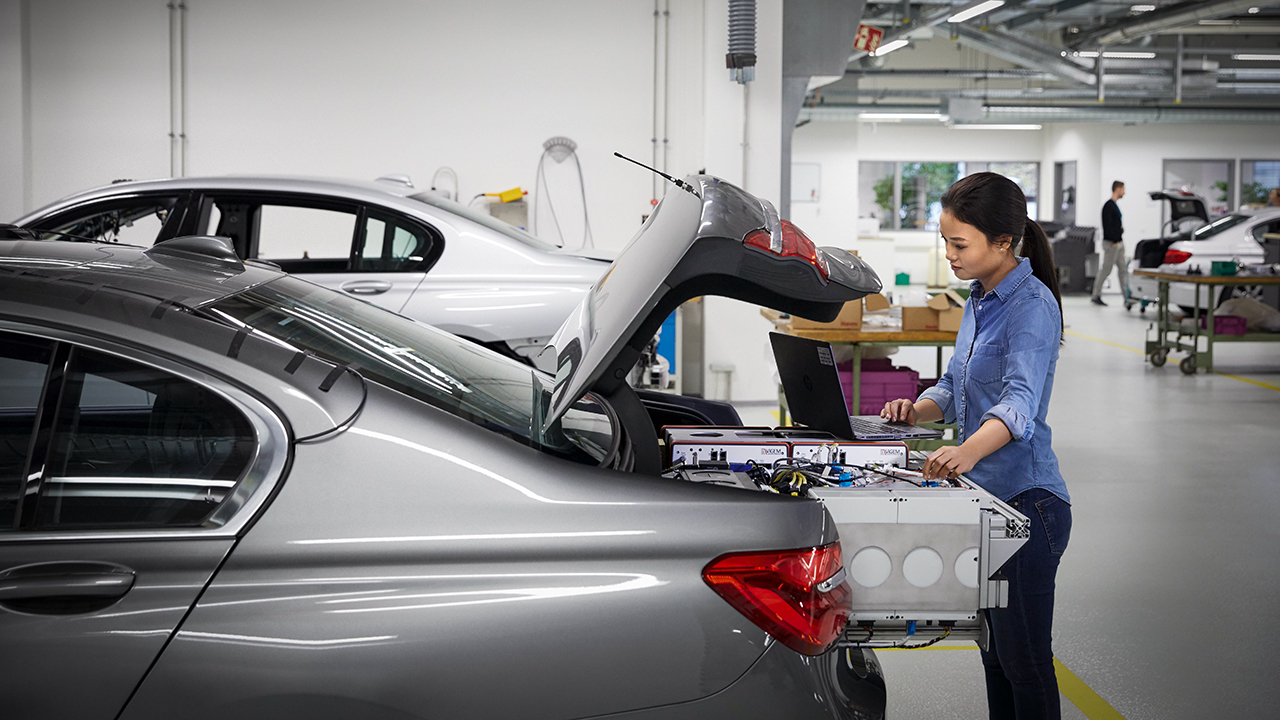 A female IT employee working on technology inside the trunk of a BMW. 