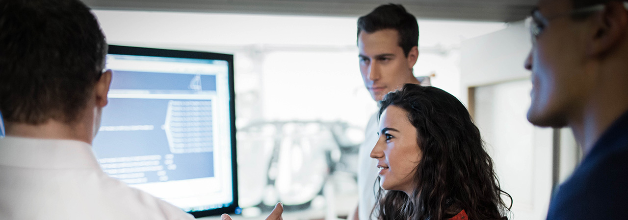Four BMW Group employees taking a look at graphs shown on a computer screen.