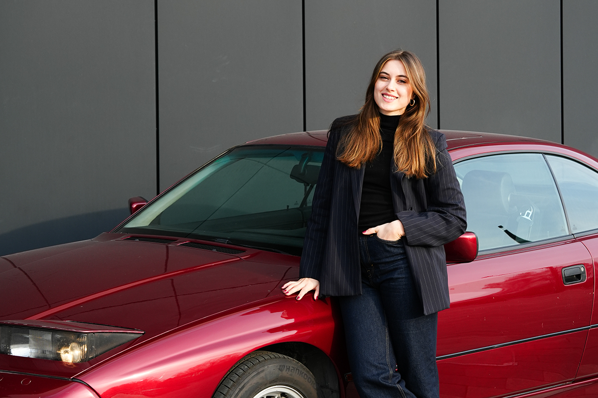 Legal intern Sonja leans against a red BMW car.