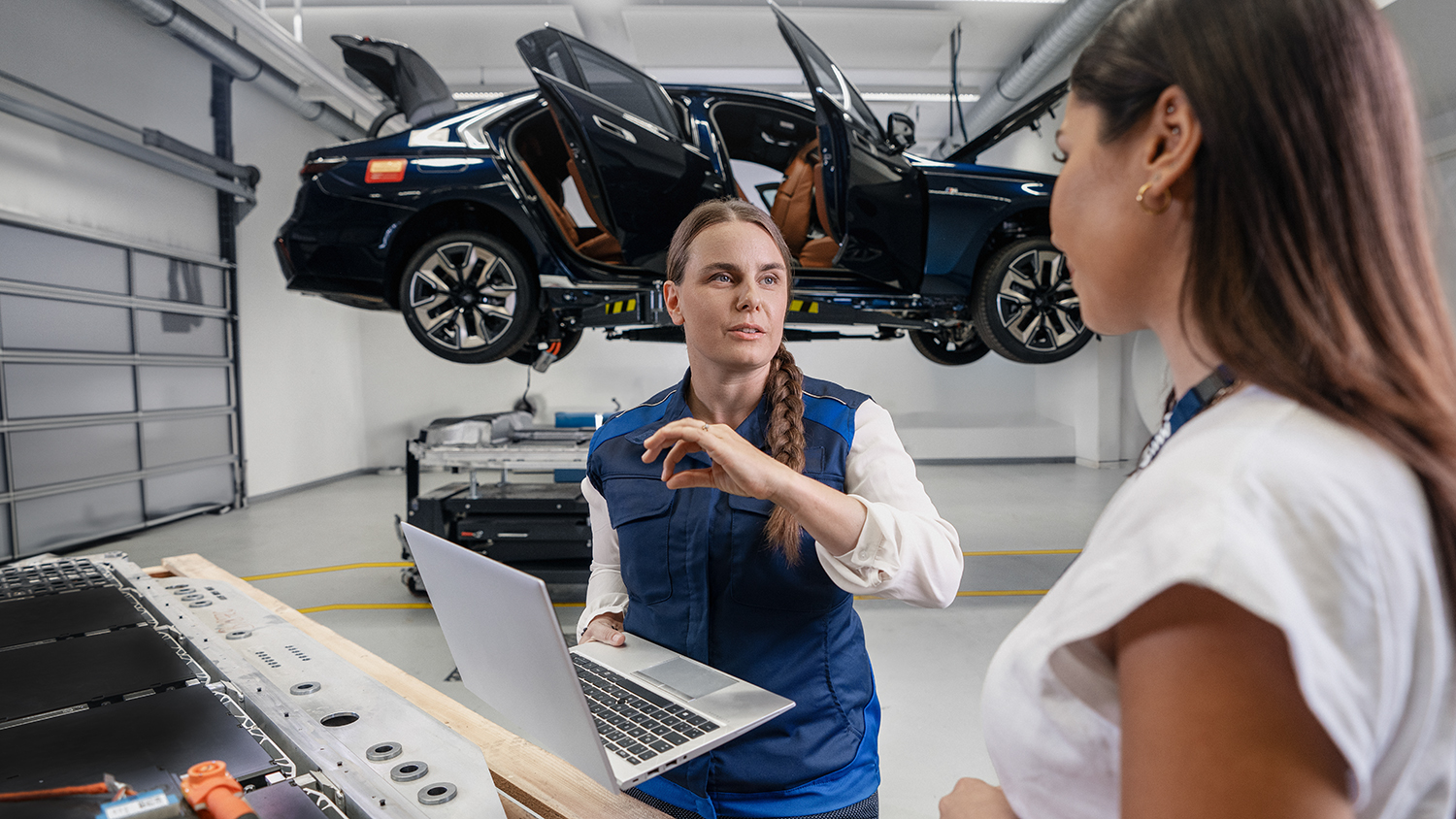 Two employees working together on a computer with a car on a lift in the background.
