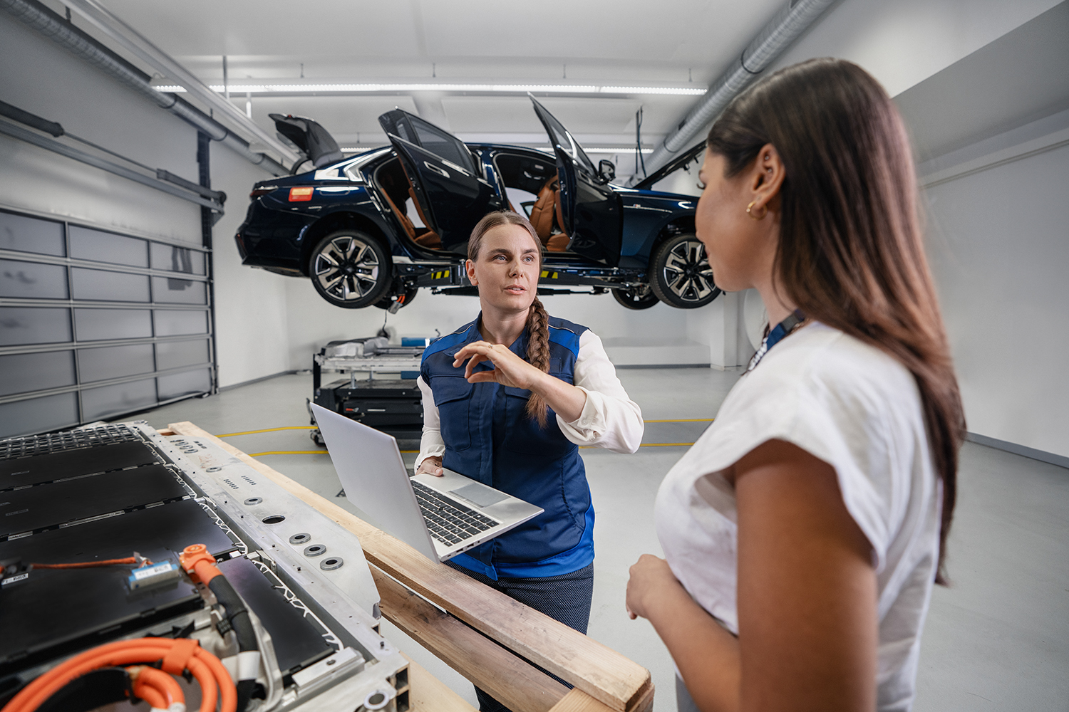 Two employees working together on a computer with a car on a lift in the background.