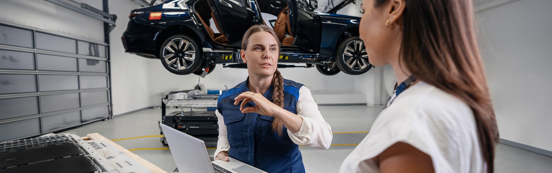 Two employees working together on a computer with a car on a lift in the background.
