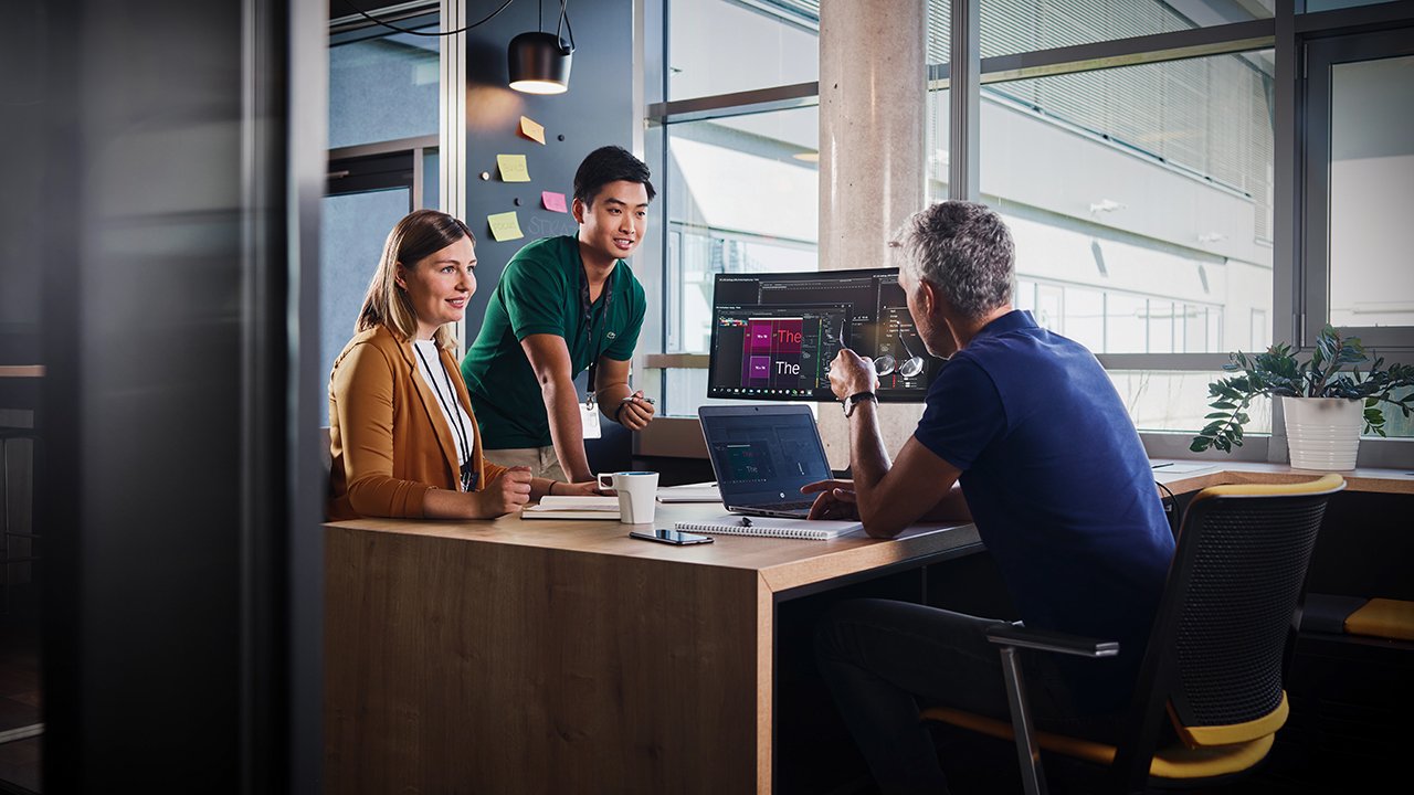 Three colleagues analysing data on a computer screen in the office.