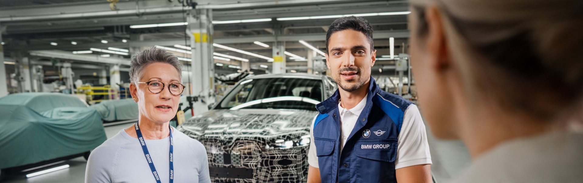 Drei BMW Group Mitarbeiter in der Produktionshalle während einer Besprechung.