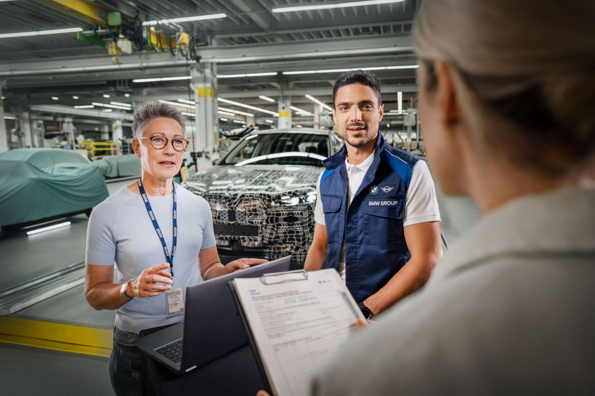 Drei BMW Group Mitarbeiter in der Produktionshalle während einer Besprechung.