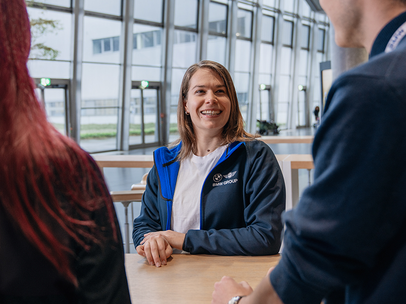 Three BMW Group employees having a conversation in a modern, open working environment.