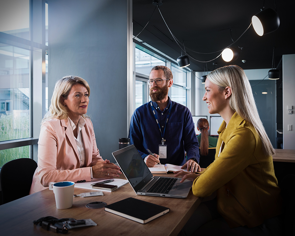 Three colleagues at the BMW Group are having a conversation in a modern office setting.