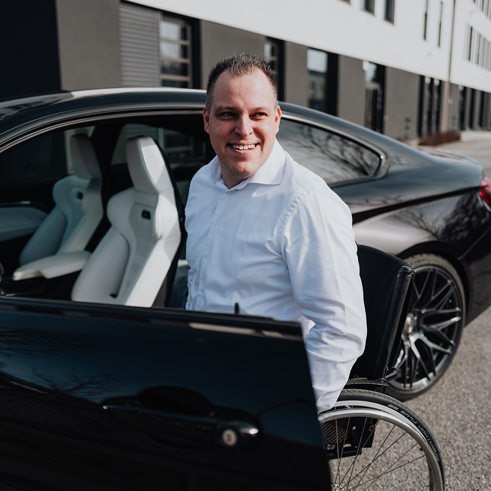 BMW Mitarbeiter Markus sitzt in seinem Rollstuhl an der geöffneten Tür seines BMW M4