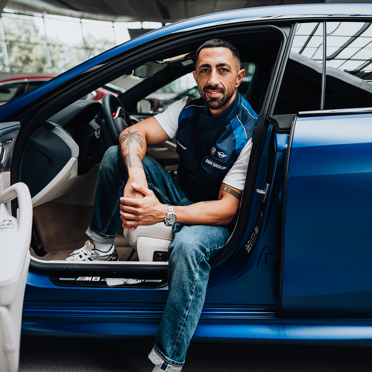 Umut sits on the drivers seat of a BMW M8. 
