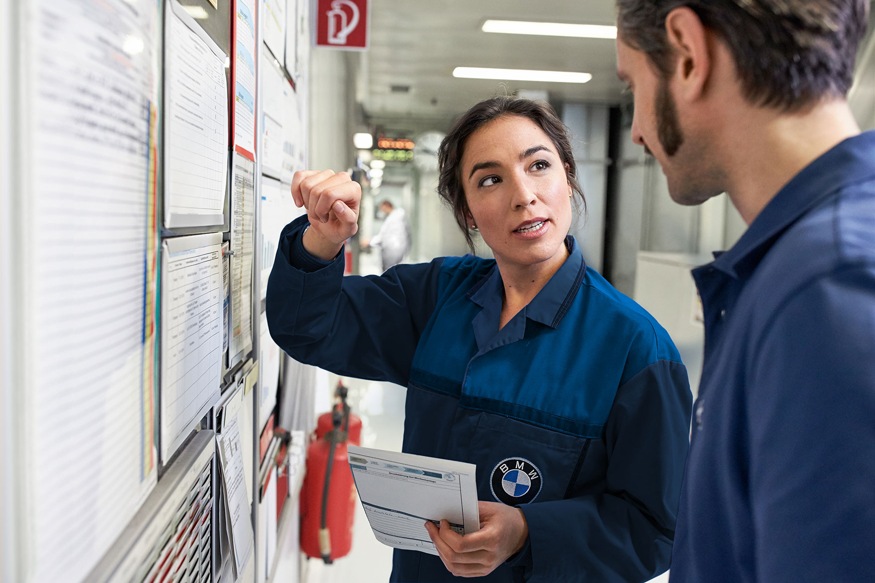 A female BMW Group employee explaining something on a pinboard to her colleague.
