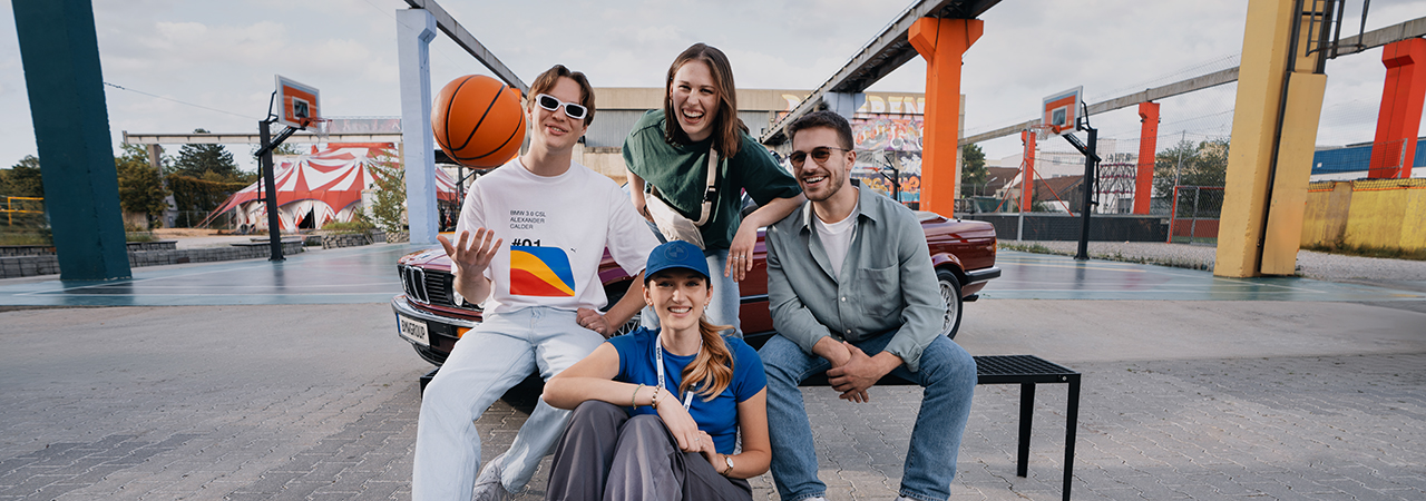 A group of four friends enjoying basketball outdoors with a vintage BMW in the background.