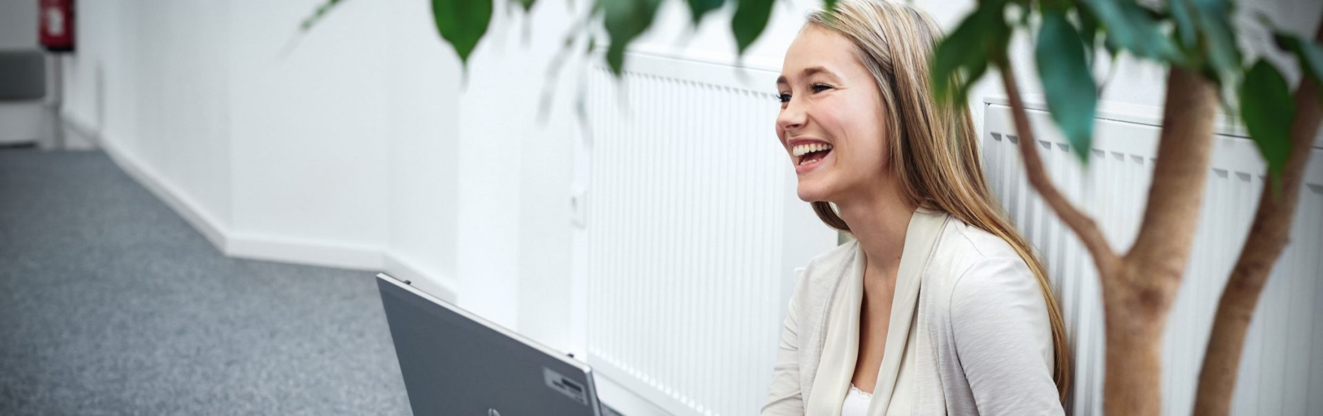 A female apprentice sits on the floor with her computer and laughes.