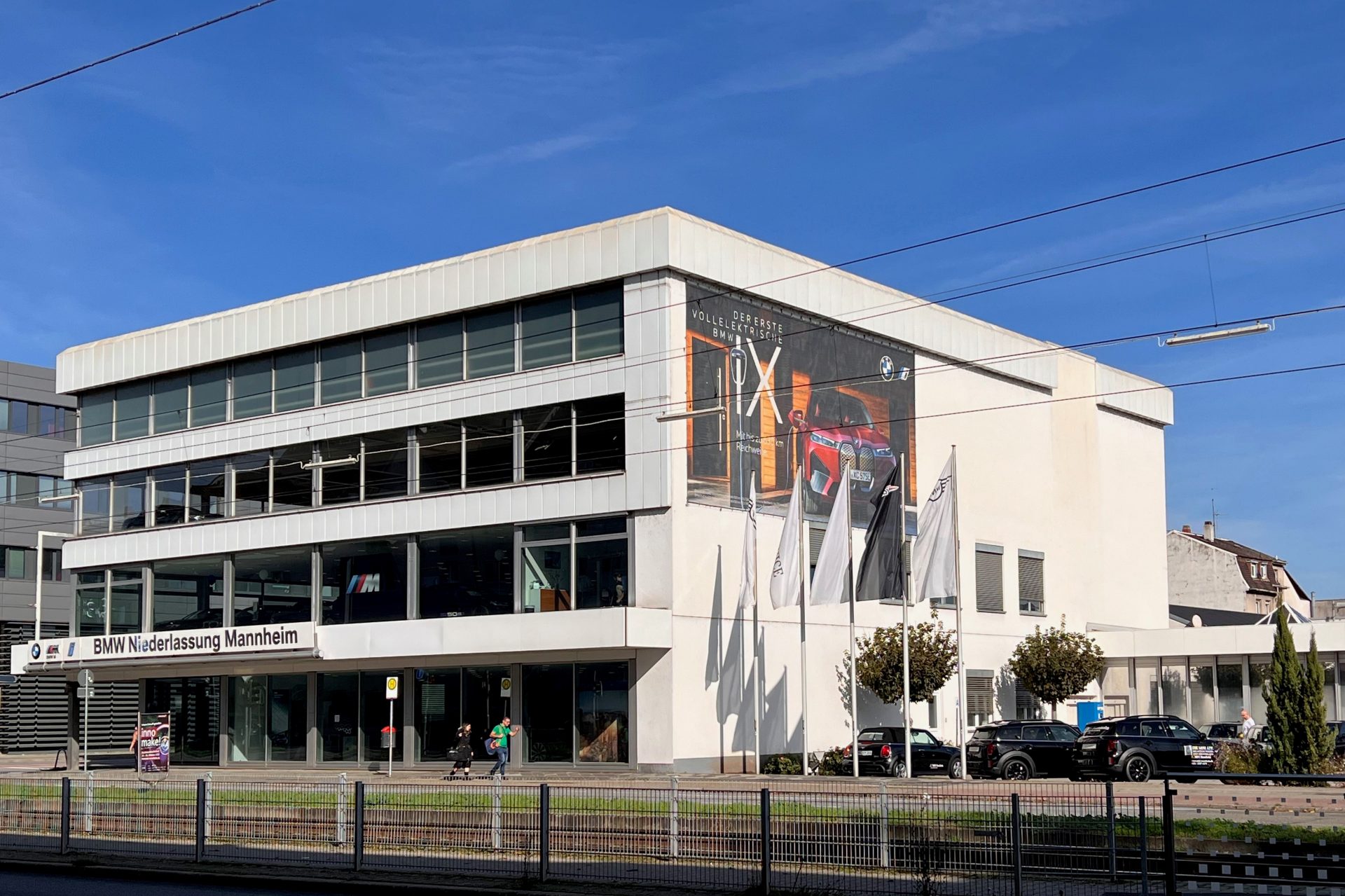 Exterior view of BMW Niederlassung Mannheim dealership with flags and cars.