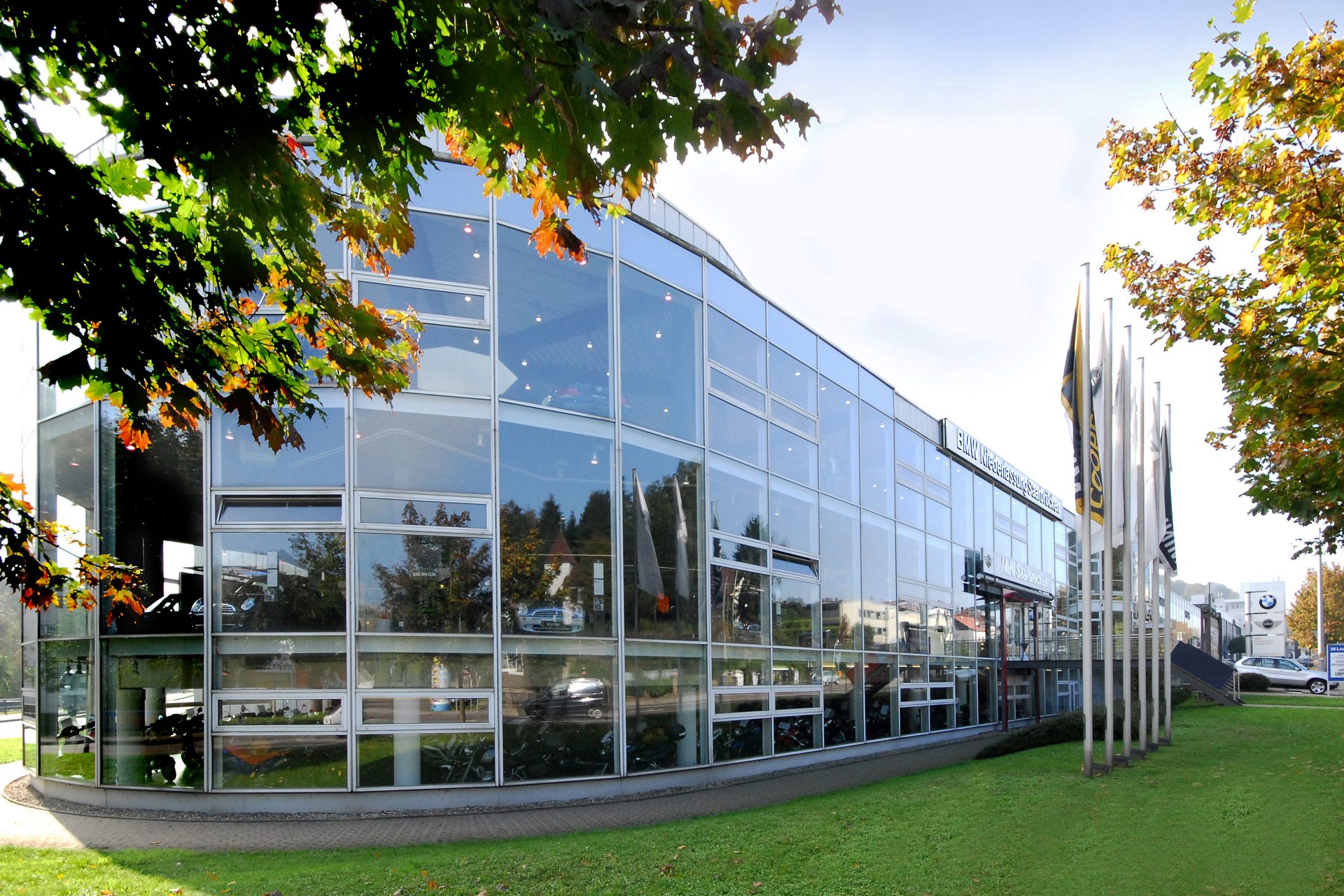 Exterior view of the modern BMW retail centre in Saarbrücken with glass facade and surrounding greenery.