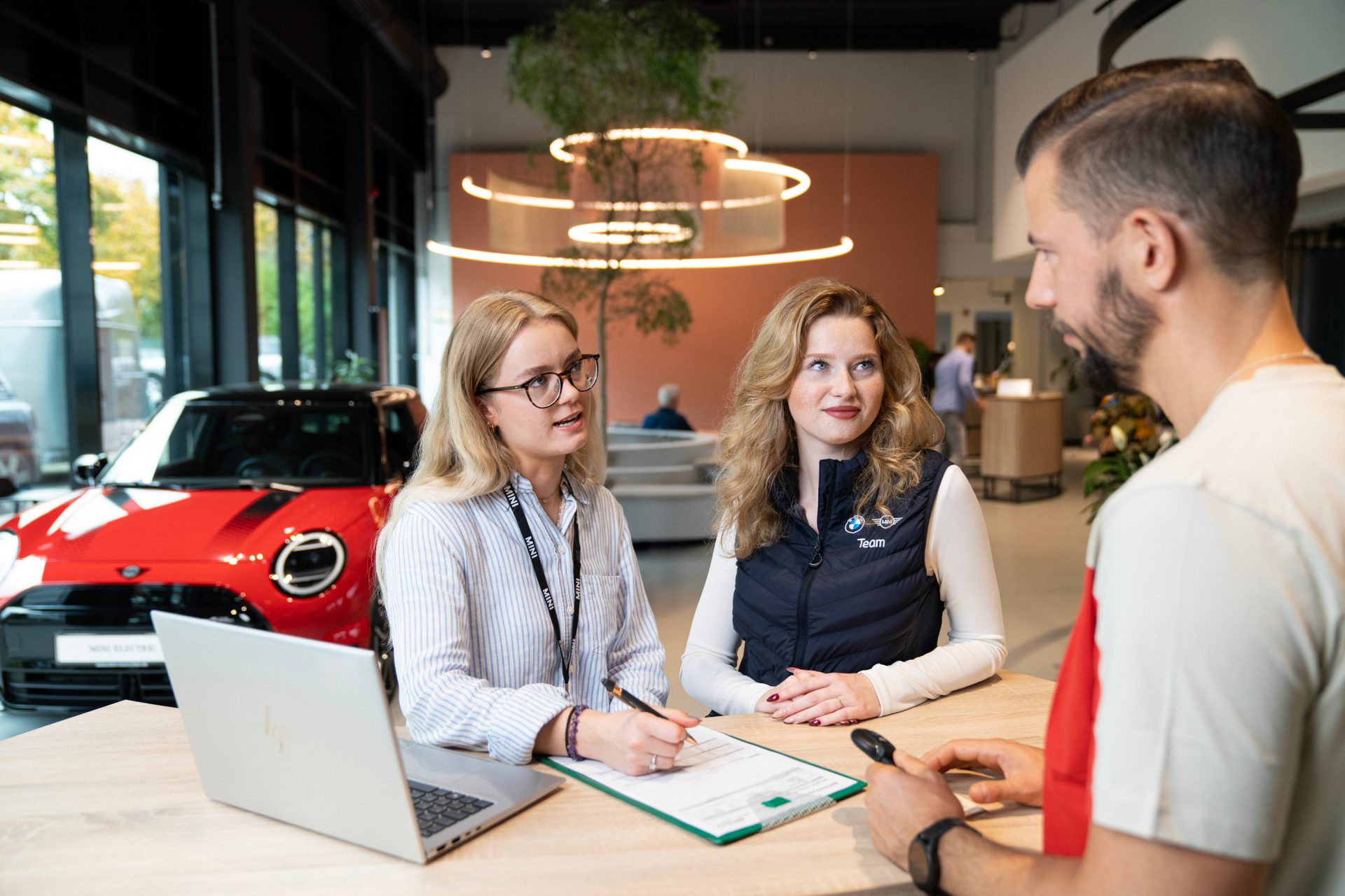 Engaging conversation between customers and sales representatives apprentices in a modern car showroom.