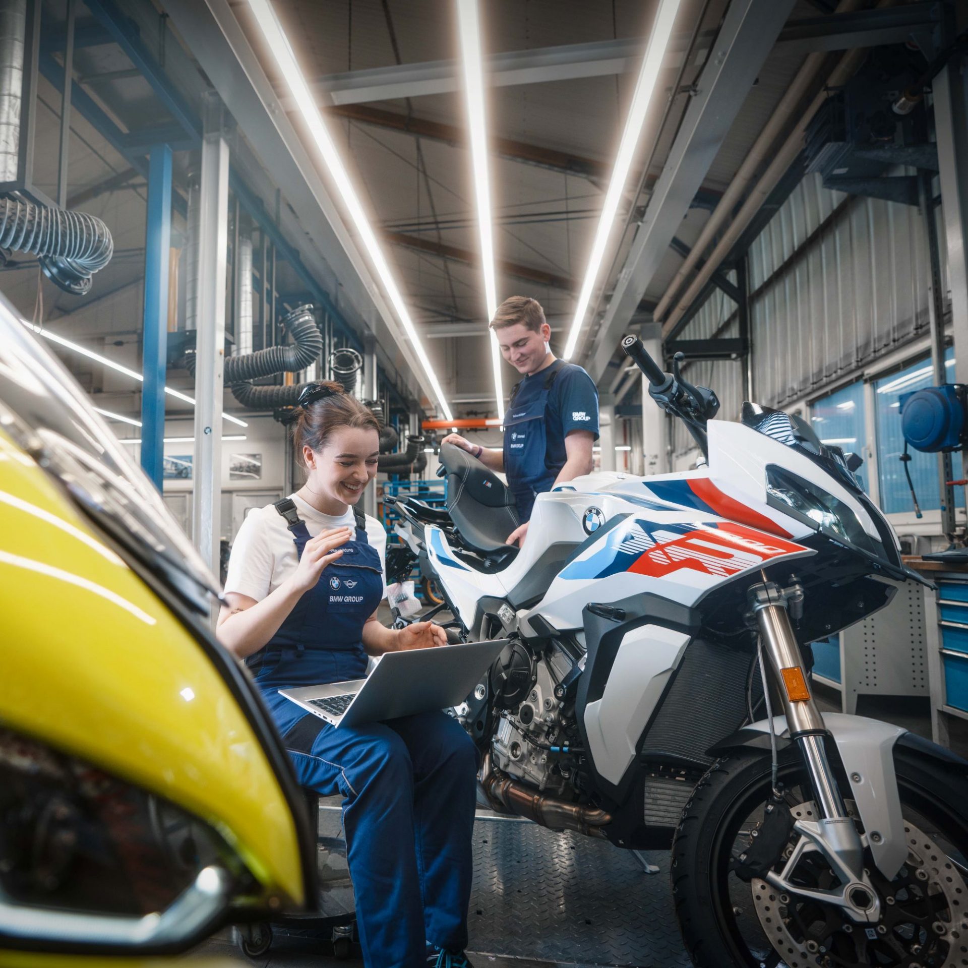 The image shows two apprentices at work in the BMW Motorrad plant Berlin.