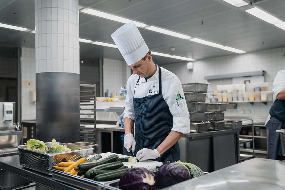 A professional cooking environment with a chef preparing food and fresh vegetables in the BMW Group Company kitchen.