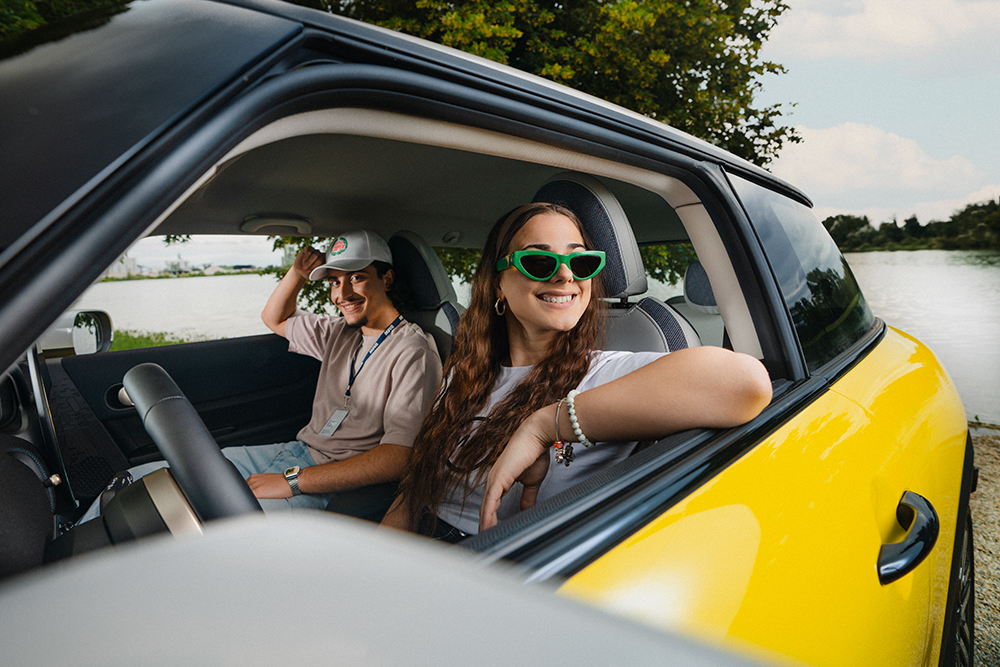 Two young apprentices at the BMW Group in a rented car on a sunny day.