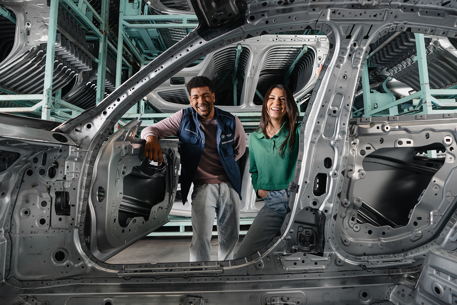 BMW Group apprentices posing next to car frames in a production facility.