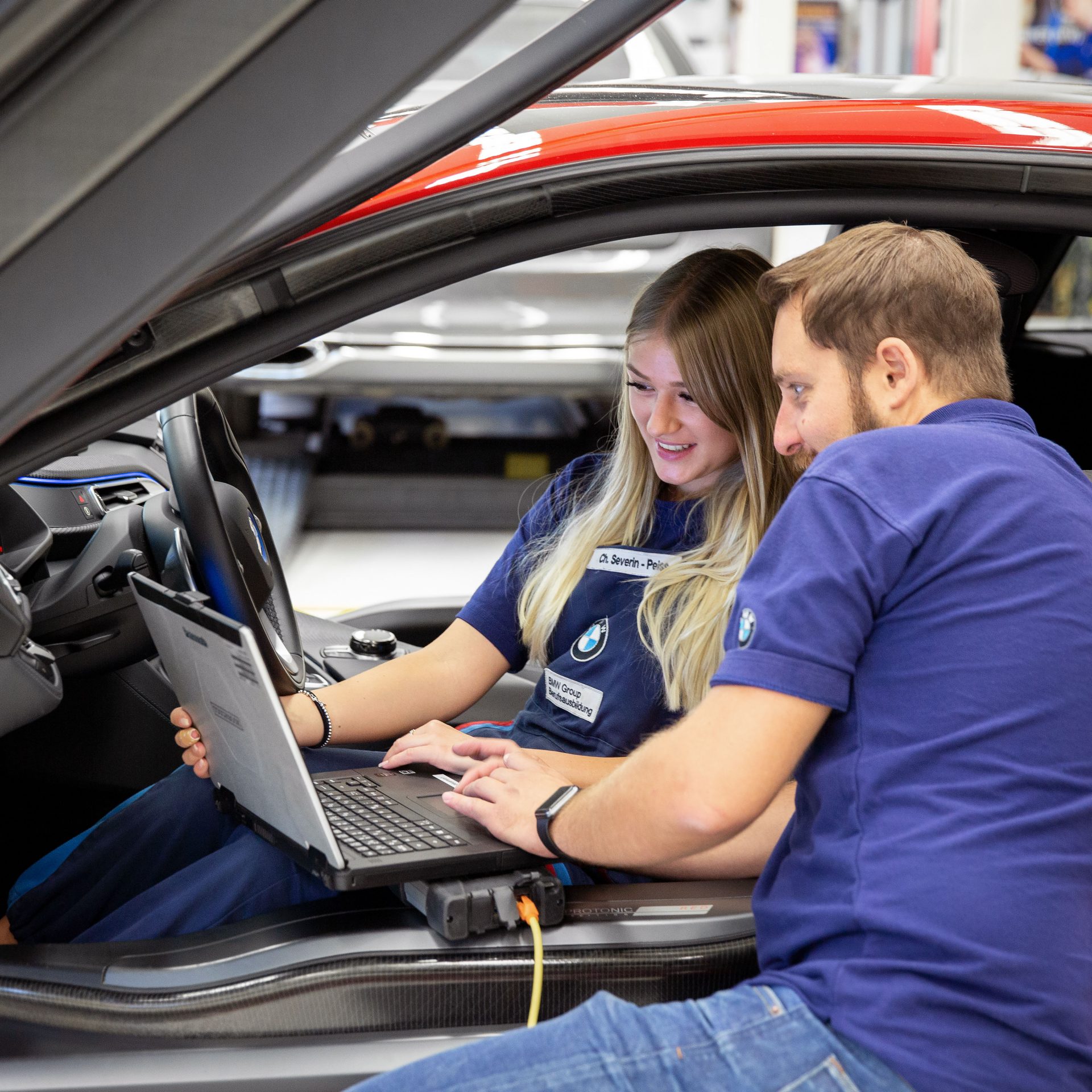 Auf dem Bild ist eine Auszubildende zur Kfz-Mechatronikerin bei BMW zu sehen, die ihrem Kollegen etwas am Laptop zeigt. 
