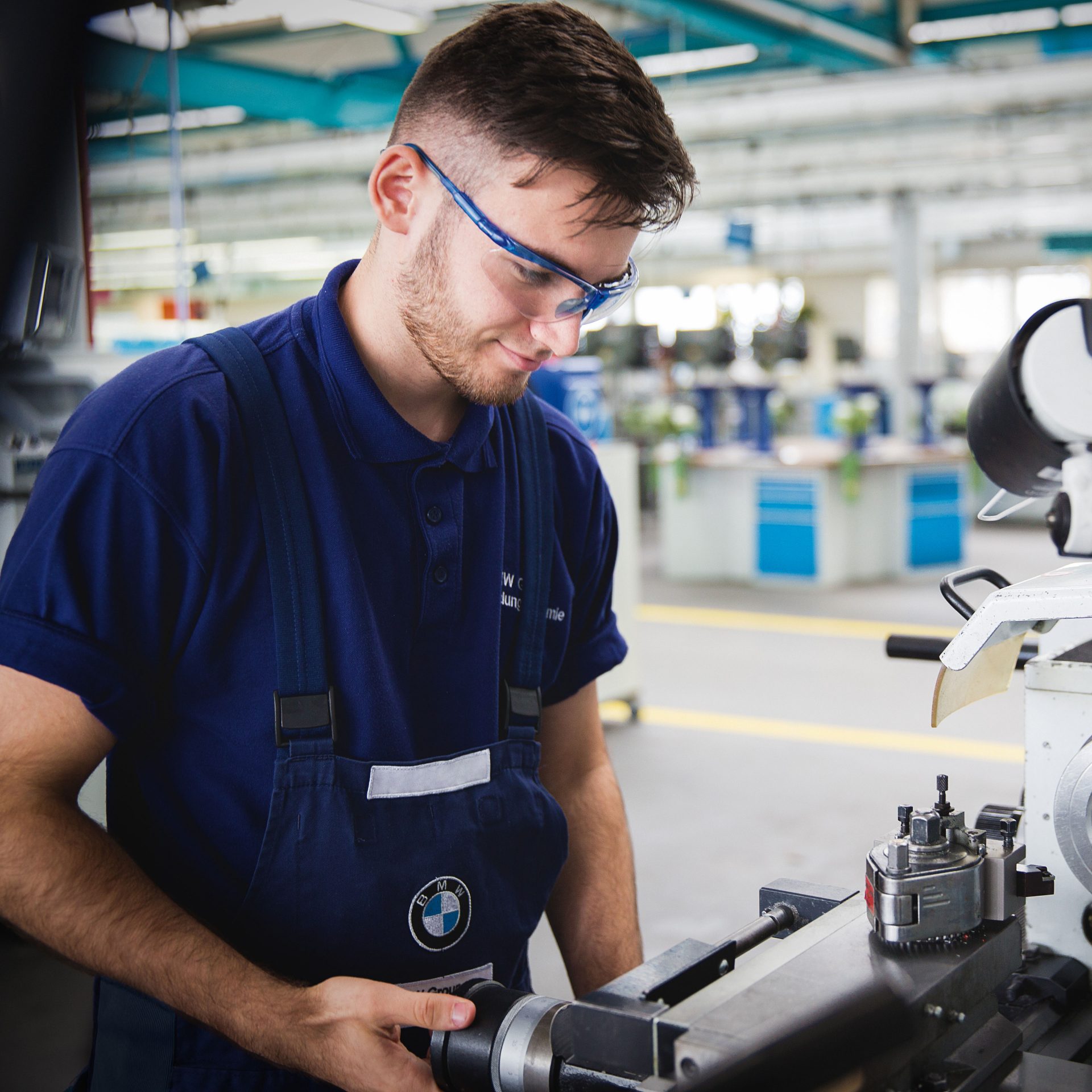 Auf dem Bild ist ein junger Auszubildender zum Mechatroniker bei BMW zu sehen, der eine Schutzbrille trägt.