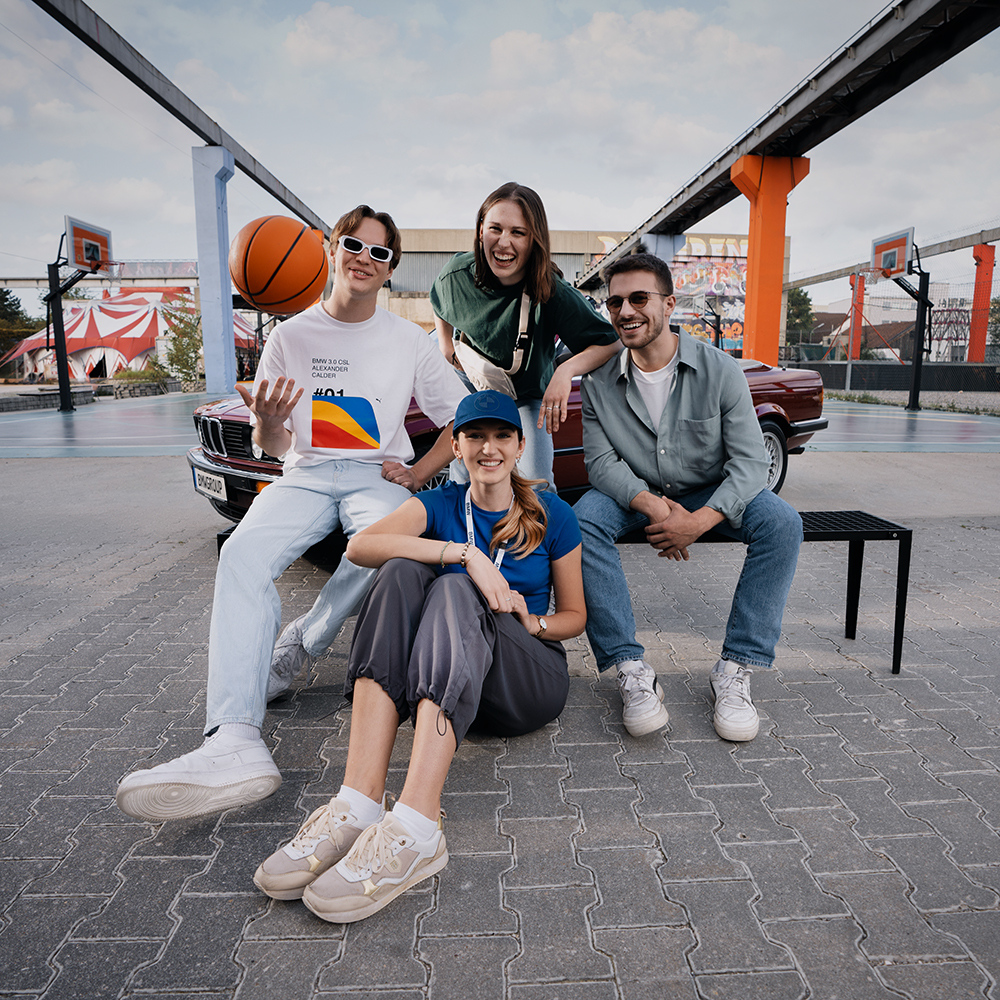 A group of four friends enjoying basketball outdoors with a vintage BMW in the background.