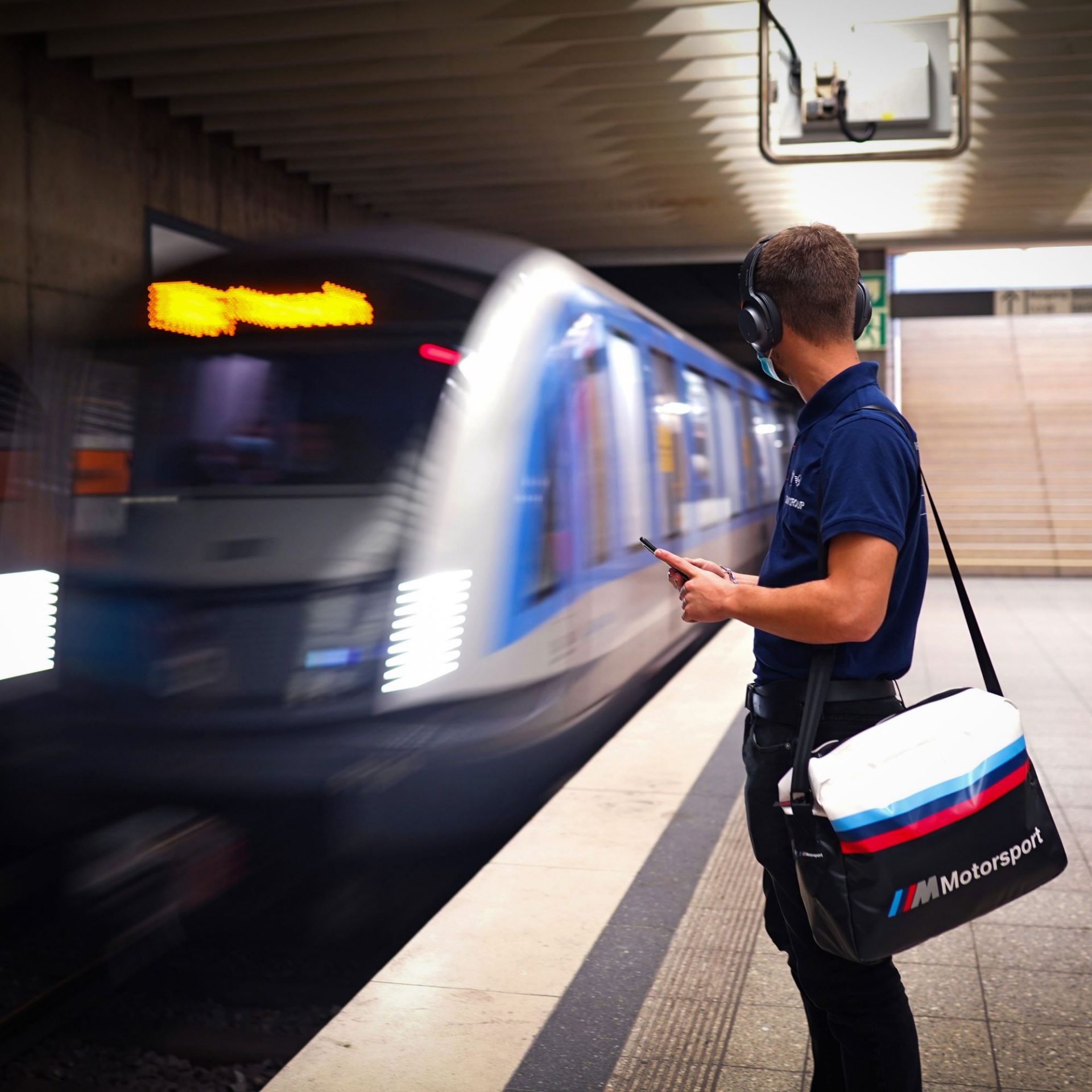 A BMW apprentice waiting for his train at a Underground station, with a blurred train in motion.