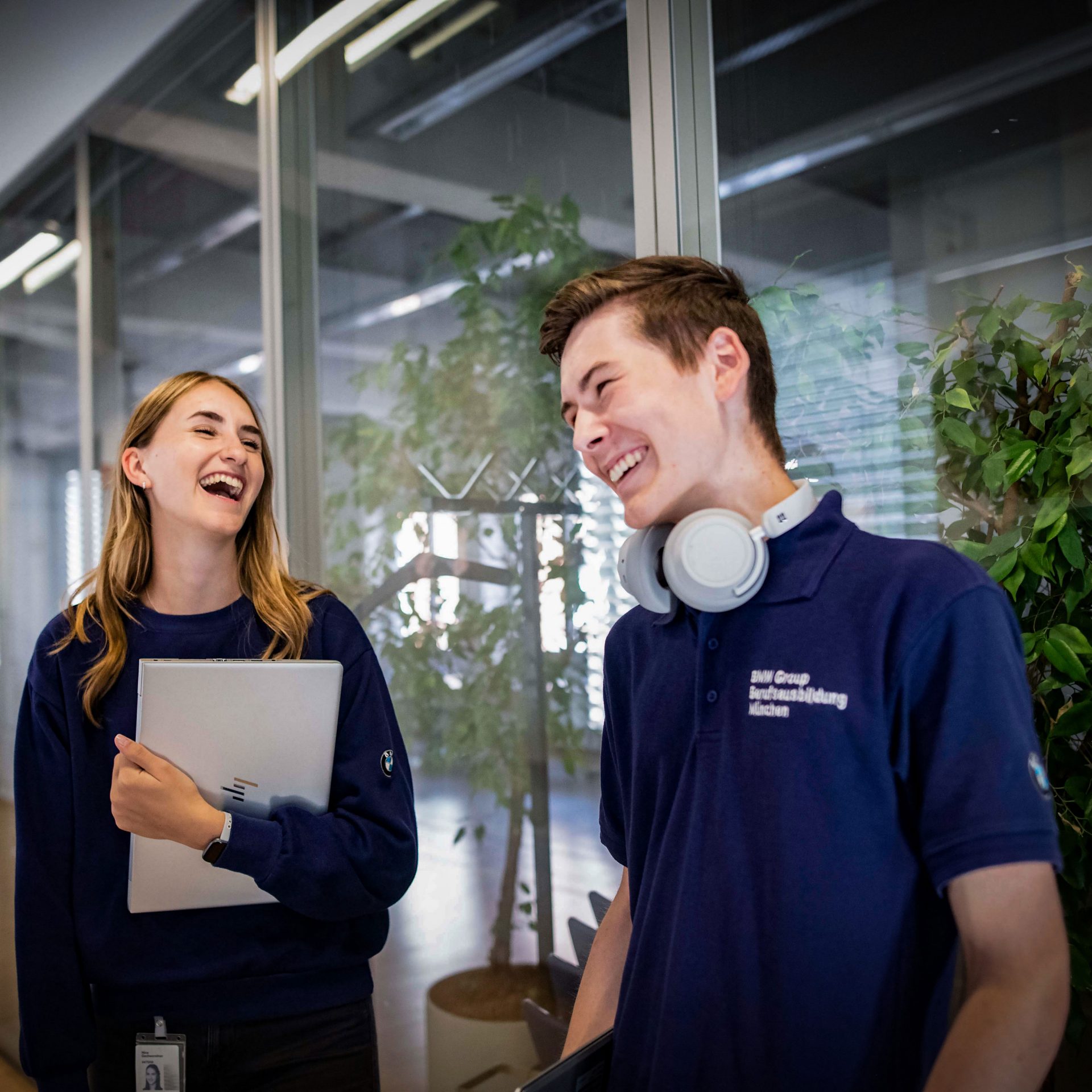 Two young BMW trainees are laughing and working together in a modern office.