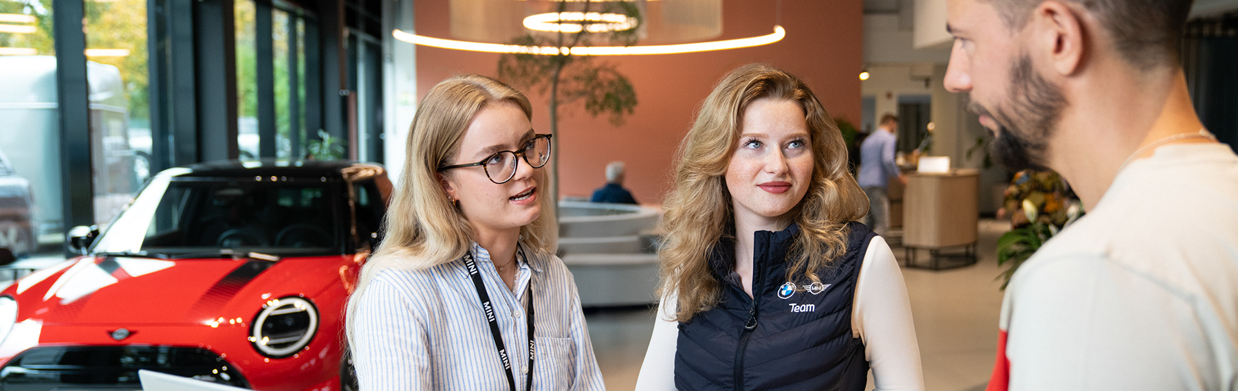 Two employees talk with a customer in a Mini dealership.